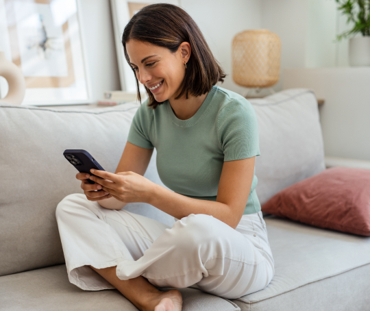 Smiling young woman sitting on a sofa, looking at her phone and enjoying a relaxed moment